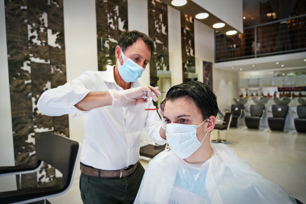 A hairdresser, wearing a protective face mask, works in a barber shop