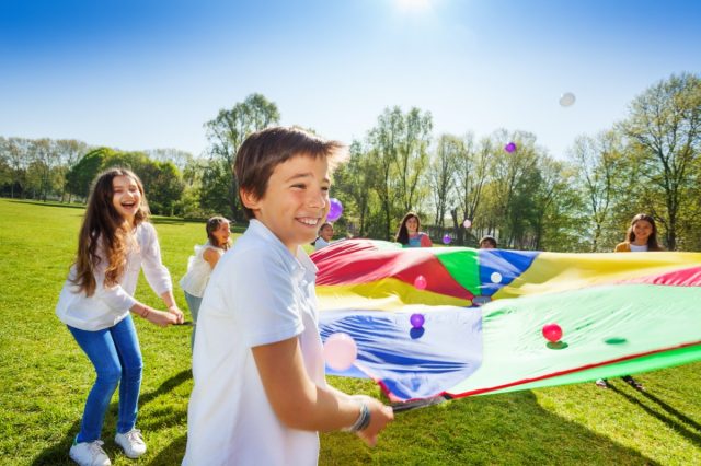 Boy throwing balls up by using rainbow parachute