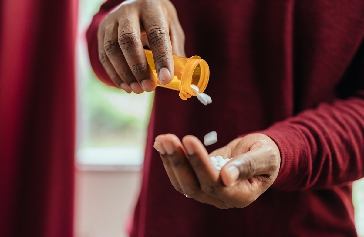 man in red shirt pouring pills from prescription pill bottle