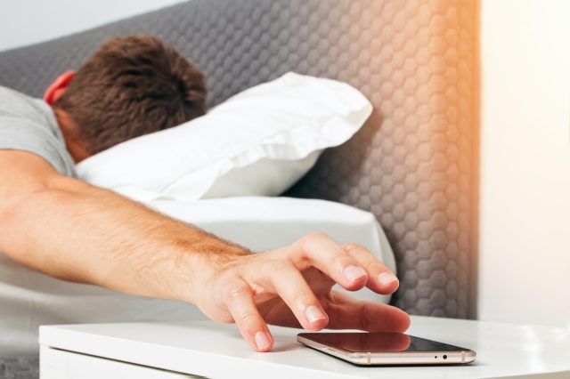 I'm a Doctor and Warn You Never Press This Button on Your Phone — Eat This Not That 27 Man's hand close-up trying to reach out ringing cell phone or alarm to have some snooze early in the morning.