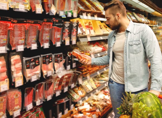man shopping for pork bacon in meat aisle and checking the label for price
