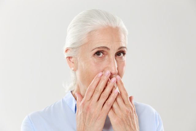 Close-up portrait of charming old lady, covering her mouth with hands