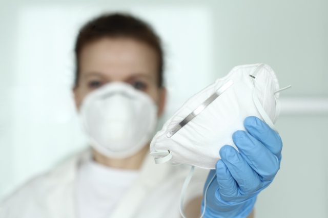 A doctor, a nurse with a face mask and blue nitride gloves sharing an N95 mask.