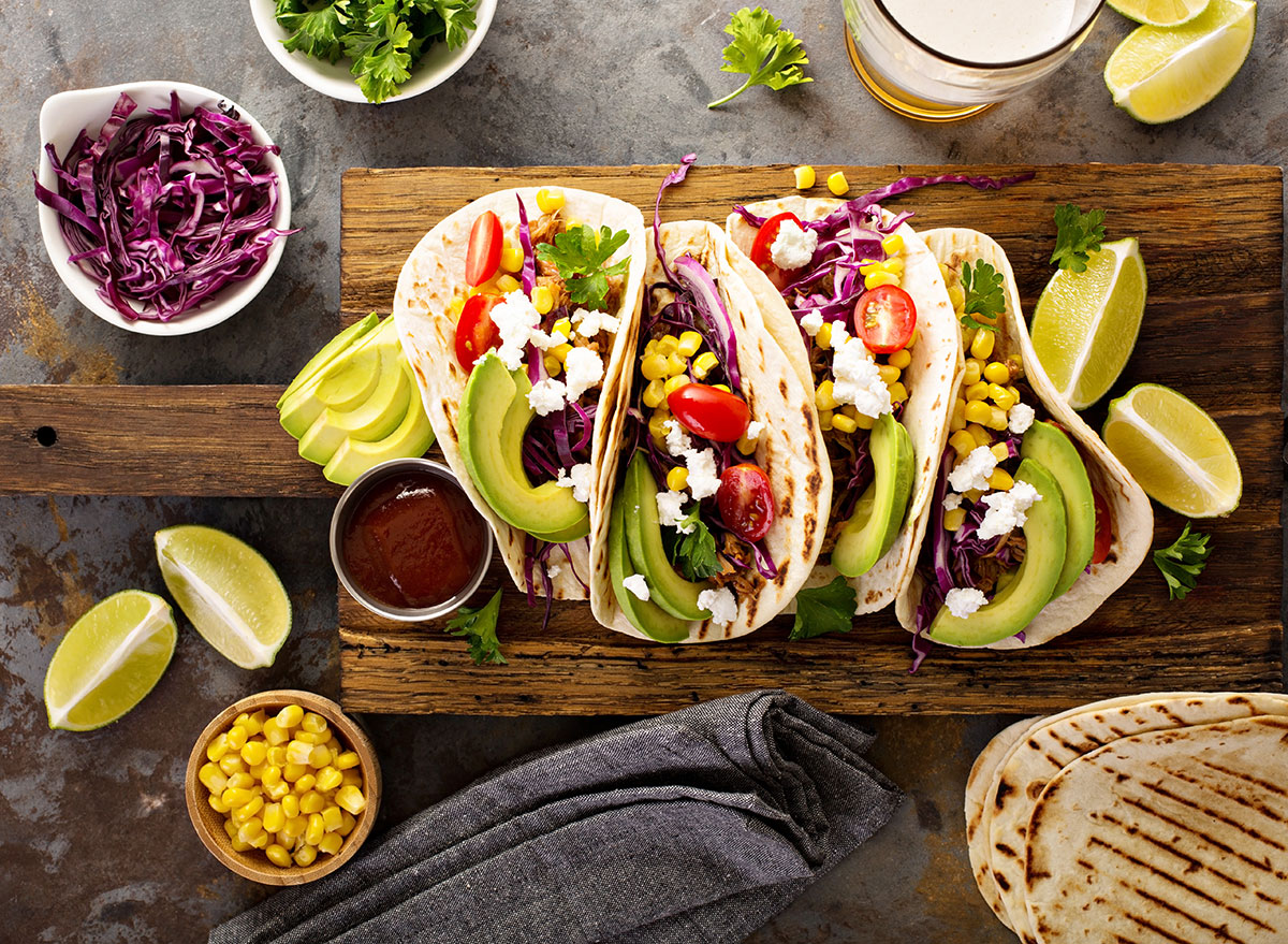 pulled pork tacos topped with avocado and cotija cheese served with lime wedges and corn