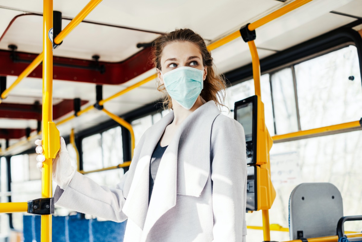 Woman wearing surgical protective mask pushing the button in a public transportation.