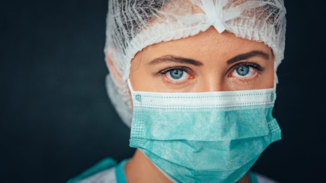 Female medical worker wearing protective face mask, head cover and suit inside hospital ward