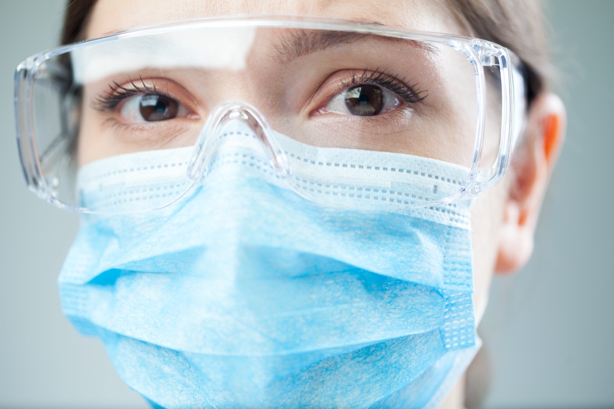 Closeup of a worried female doctor or lab scientist wearing safety glasses and blue face mask