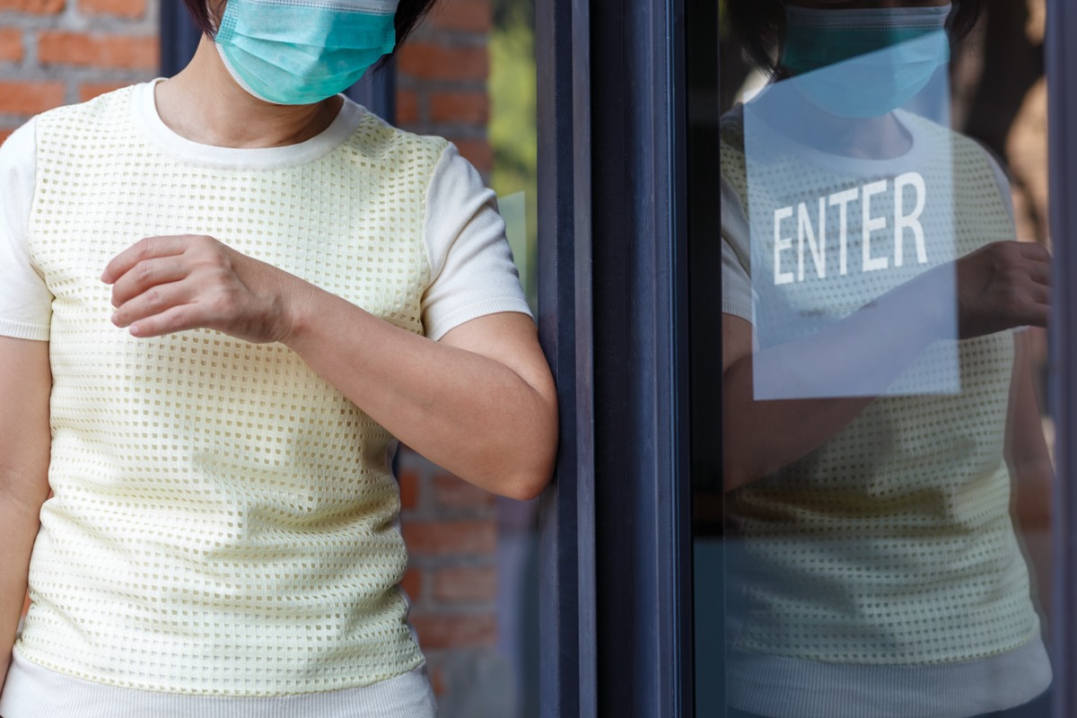 Woman wearing mask opening the door with the elbow for protection infection COVID-19