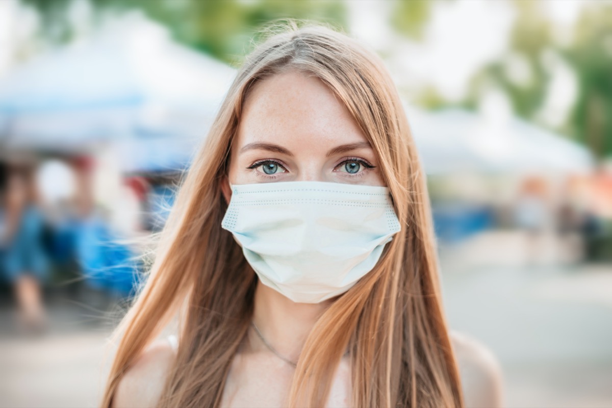 Portrait of a young Caucasian girl wearing a white medical mask on a background of nature and cityscape, coronavirus, air pollution concept