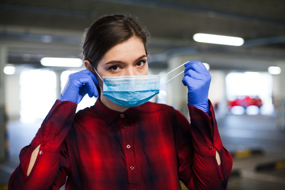 Young caucasian woman wearing surgical gloves putting face mask on, protection from spread of Coronavirus