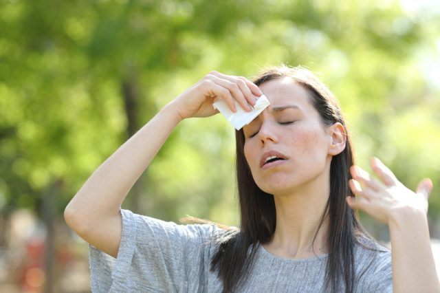 Stressed woman drying sweat using a wipe in a warm summer day in a park