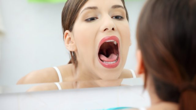 Woman stands about a mirror in a bathroom with open mouth.