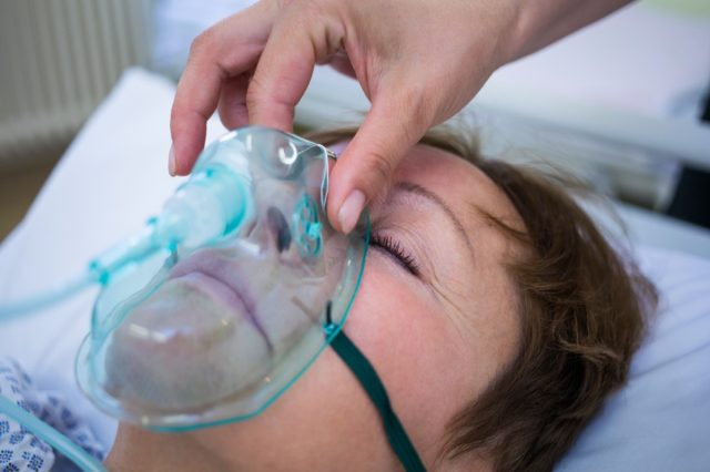 Nurse placing an oxygen mask on the face of a patient in hospital.