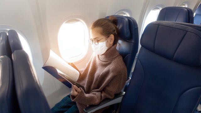 A young woman wearing face mask is traveling on airplane , New normal travel after covid-19 pandemic
