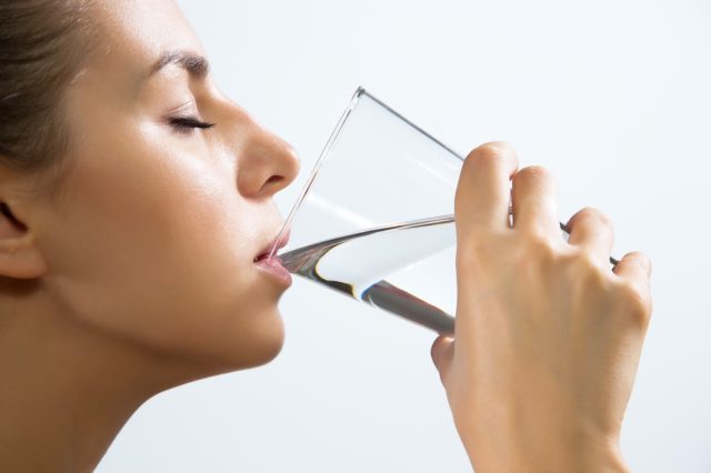 A close-up of a beautiful young woman drinking water from a glass