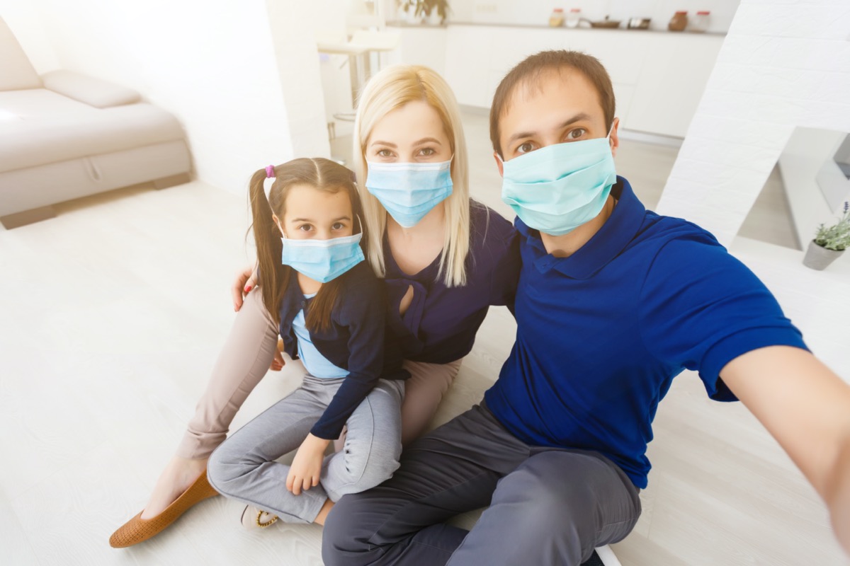 family with dad, mom and daughter staying at home wearing facial masks