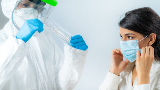 Medical worker in protective suite taking a swab for corona virus test, potentially infected young woman
