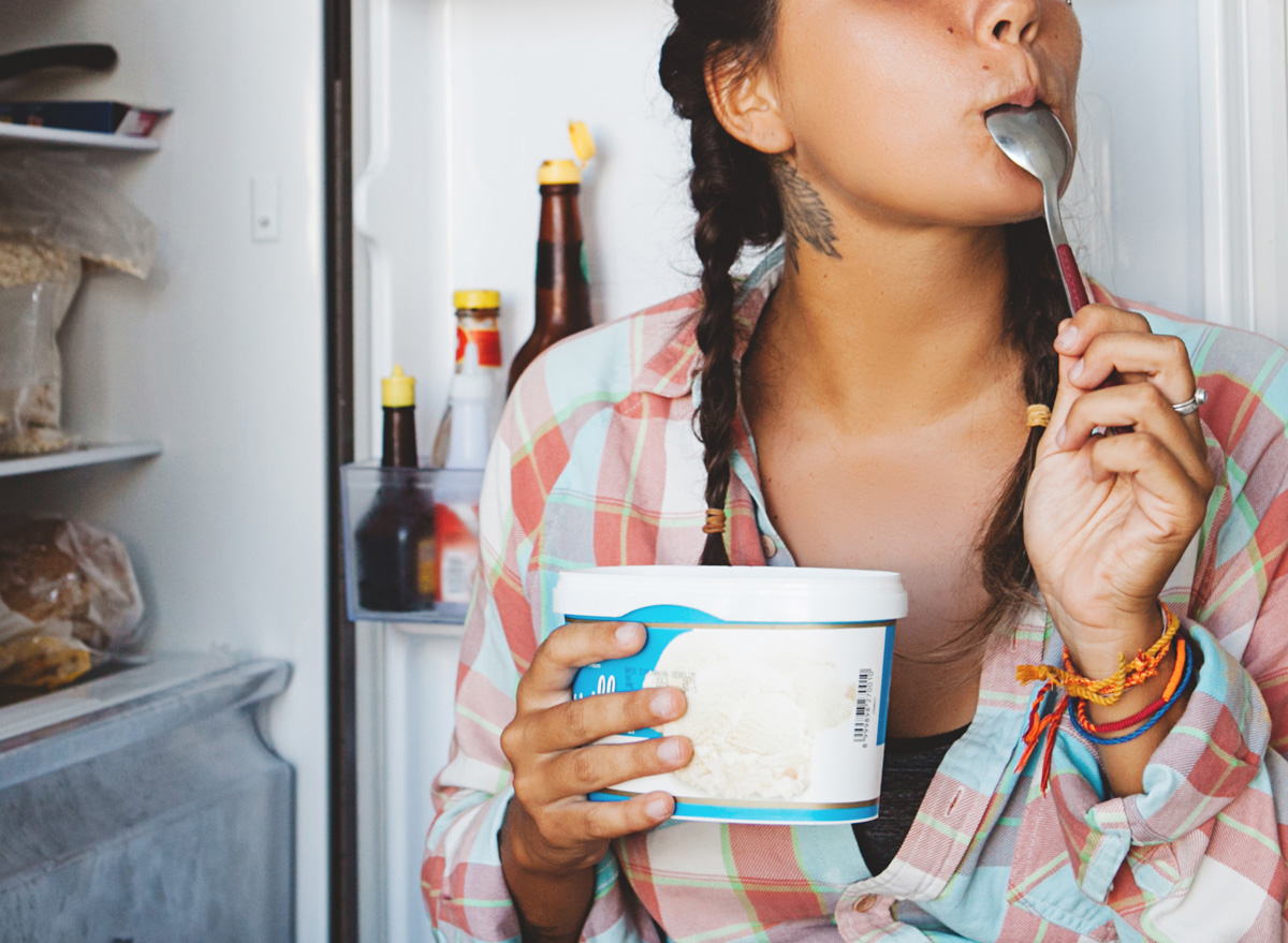 woman eating ice cream directly out of the pint and in front of the freezer