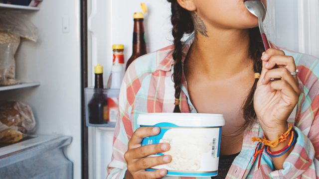 woman eating ice cream directly out of the pint and in front of the freezer