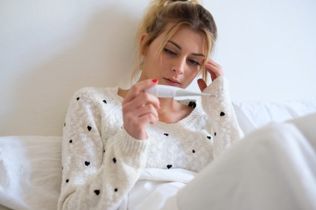 Sick woman with fever checking her temperature with a thermometer at home