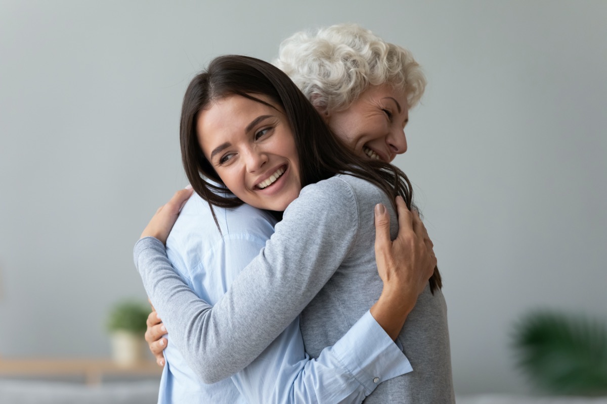 Happy young lady adult daughter granddaughter visiting embracing hugging old senior retired grandmother cuddling