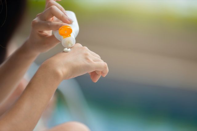 Kadın elleri ellerine güneş kremi döküyor ve boş güneş kremi tutan UV koruyucu losyon şişesi tasarımınız için kozmetik şablonu ambalajlıyor ve içeriğinizi eklemek için yer bırakıyor