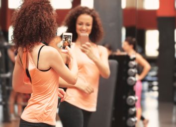 Woman taking mirror selfie at a gym showing off her weight loss