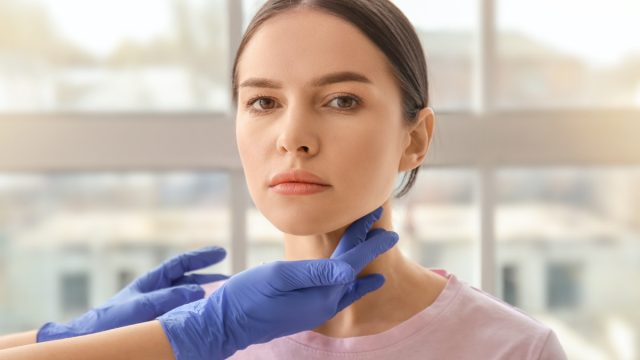 Endocrinologist examining thyroid gland of young woman in clinic