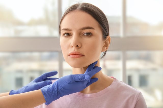 Endocrinologist examining thyroid gland of young woman in clinic