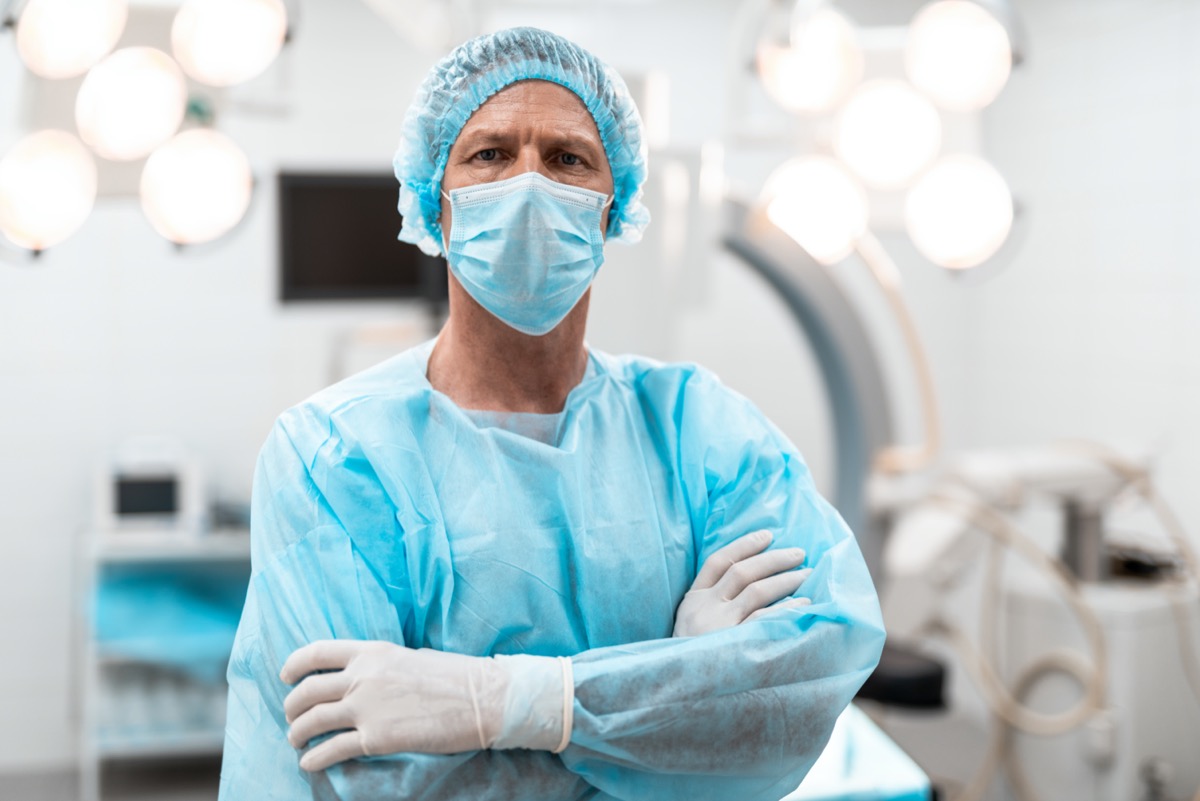 Confident experienced doctor in blue medical uniform frowning while standing with his arms crossed
