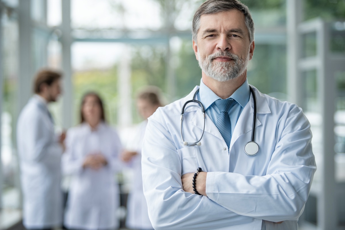 Confident smiling doctor posing in the hospital with medical team working on the background