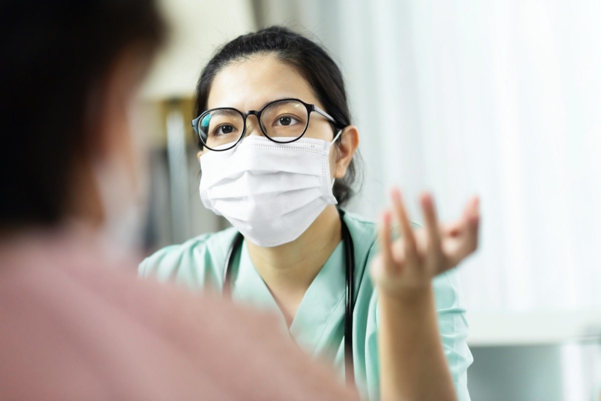 female doctor in green uniform wears glasses and surgical mask talking, consulting and giving advice to senior female patient in hospital