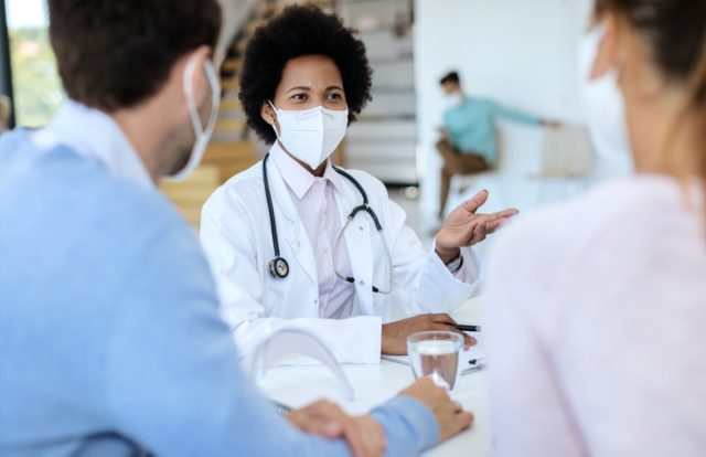 doctor wearing protective face mask while talking to her patients during an appointment