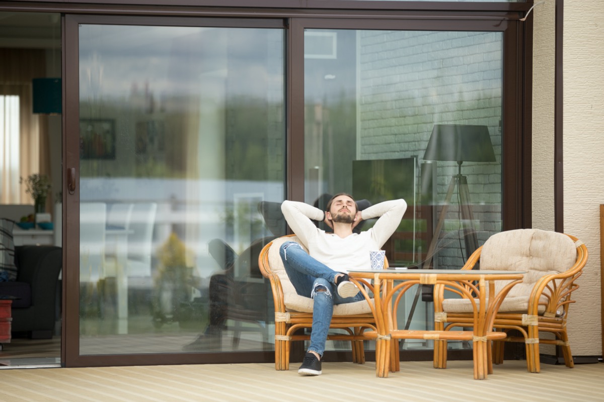 man relaxing sitting on terrace chair hands behind head