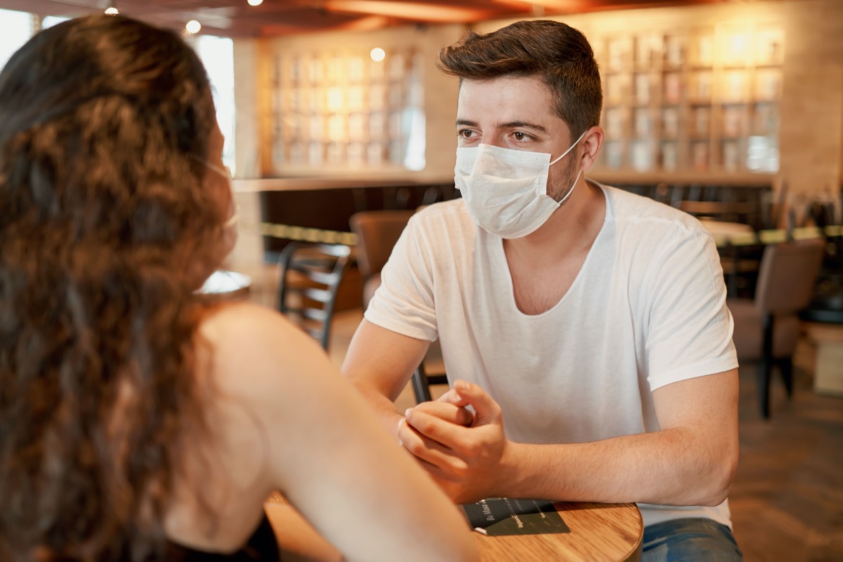 Two people wearing surgeon masks is sitting in a cafe and chatting