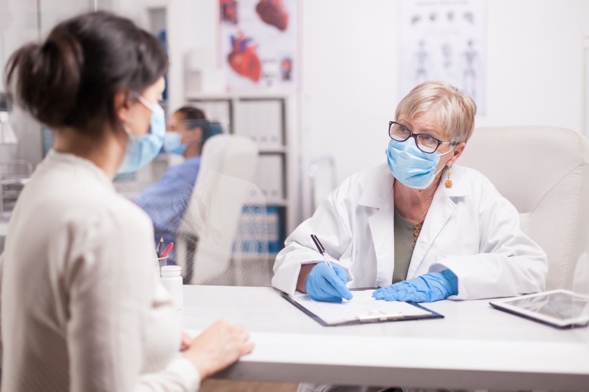 Doctor wearing protection mask against covid taking notes during consultation with patient in medical clinic