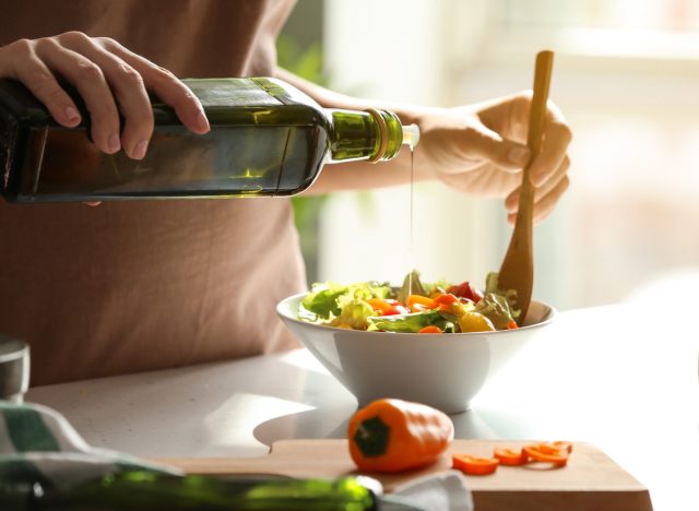 pouring extra virgin olive oil on a veggie salad