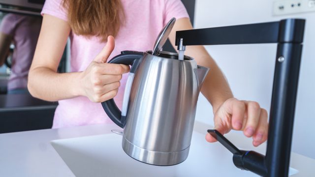 Pouring tap water into a tea kettle to boil