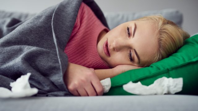 Woman suffering from cold, virus lying on the sofa under the blanket
