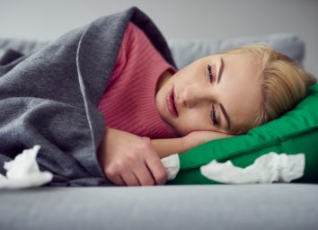Woman suffering from cold, virus lying on the sofa under the blanket