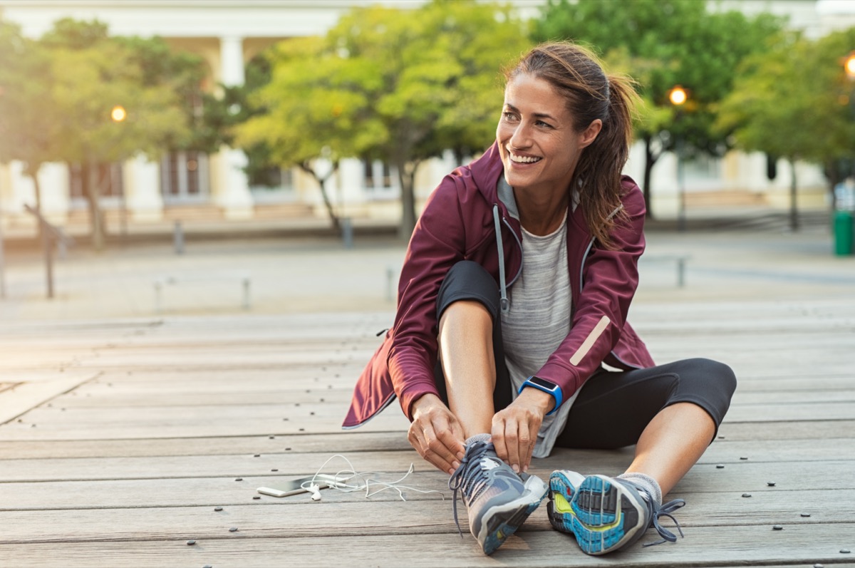 Mature fitness woman tie shoelaces on road