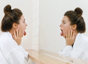 Young woman is looking on her tongue in the mirror