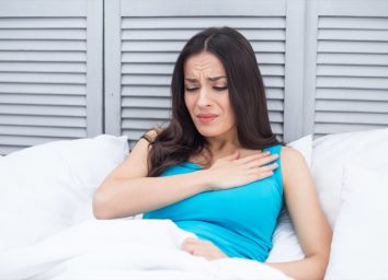 Woman lying in bed at home holding a hand to her chest by a sharp pain