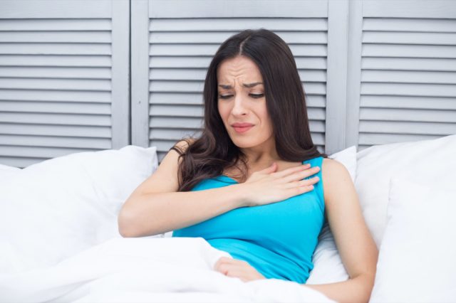 Woman lying in bed at home holding one hand on her chest in acute pain