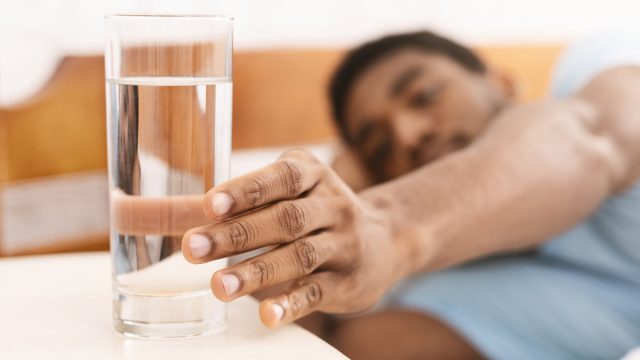 Black man reaching for a glass of water from his bed in the morning