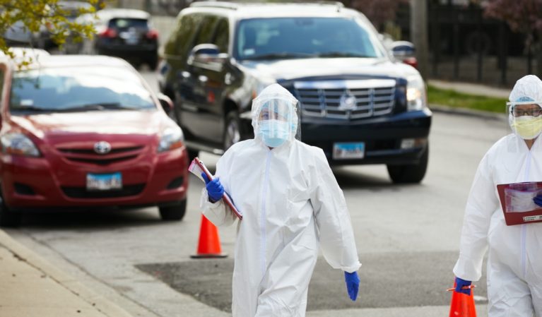 A technician at a drive up testing facility in Chicago walks between cars with patients awaiting testing for coronavirus covid-19