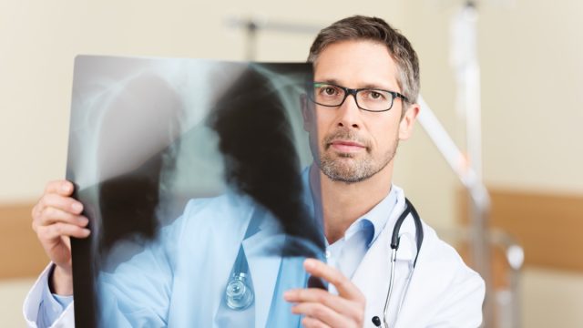 Portrait of serious mature doctor holding X-ray report in hospital