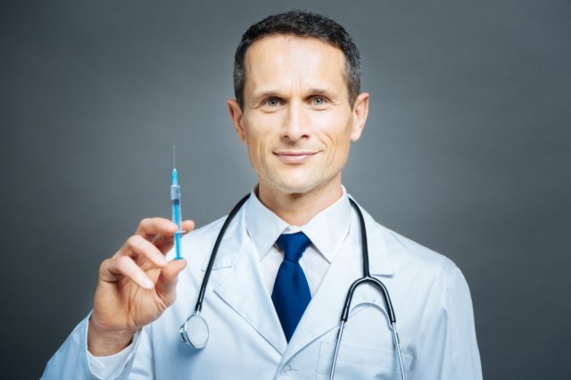 Cheerful practitioner holding syringe and smiling
