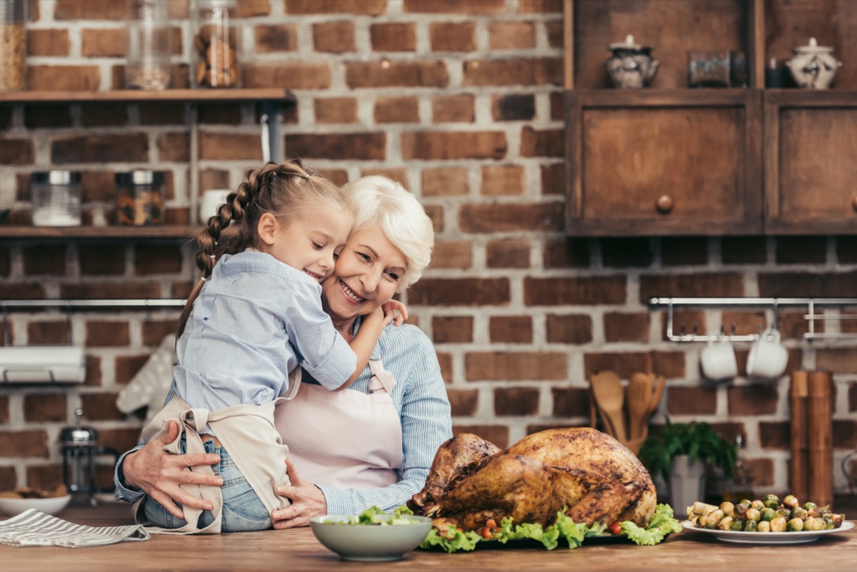 grandmother and granddaughter embracing on kitchen and looking at freshly prepared turkey for thanksgiving dinner