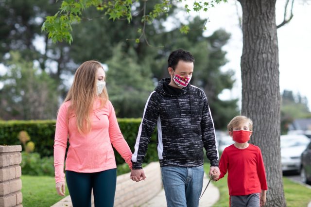 Una famiglia che cammina tenendosi per mano indossando maschere per il viso in mezzo alla pandemia